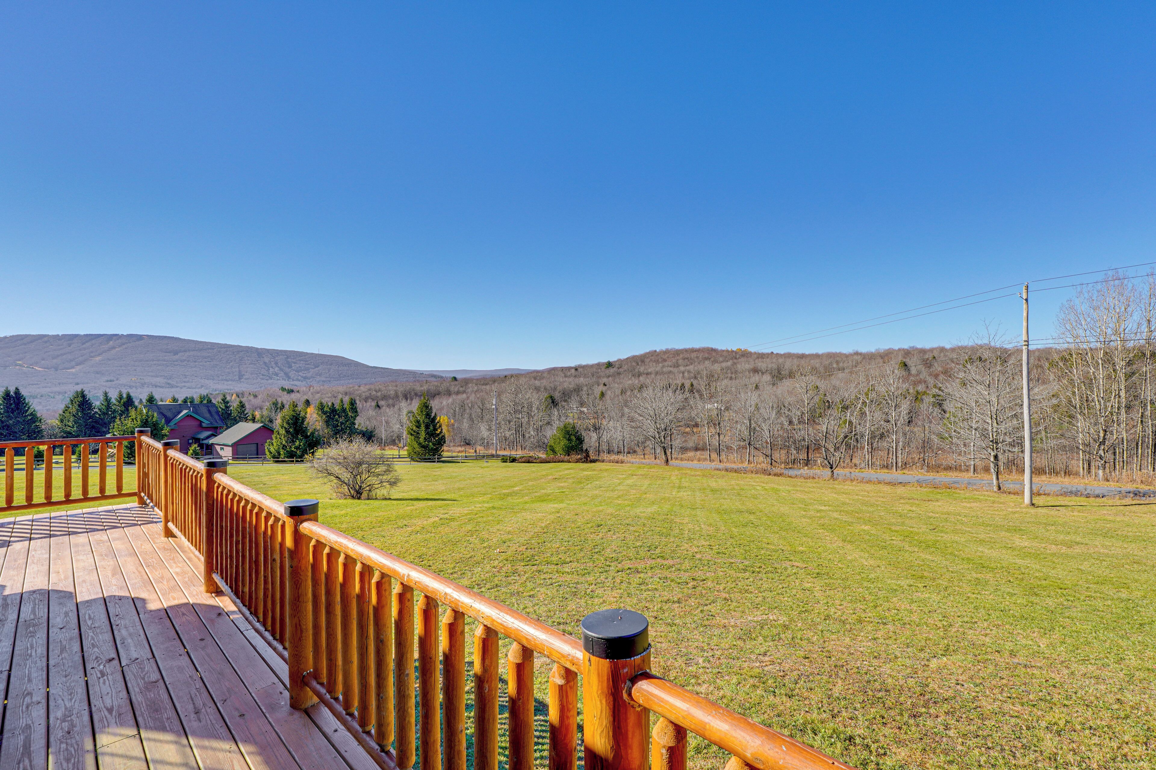 A wooden deck with a railing overlooking a grassy field and distant hills.