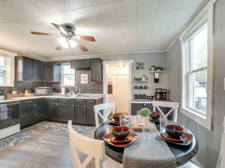 A modern kitchen with dark cabinets, a dining area with a round table, and a ceiling fan.