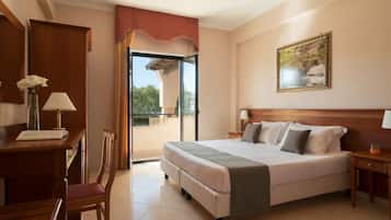 Una camera d'albergo con un letto, una scrivania, una sedia, un balcone con vista e un quadro appeso al muro.