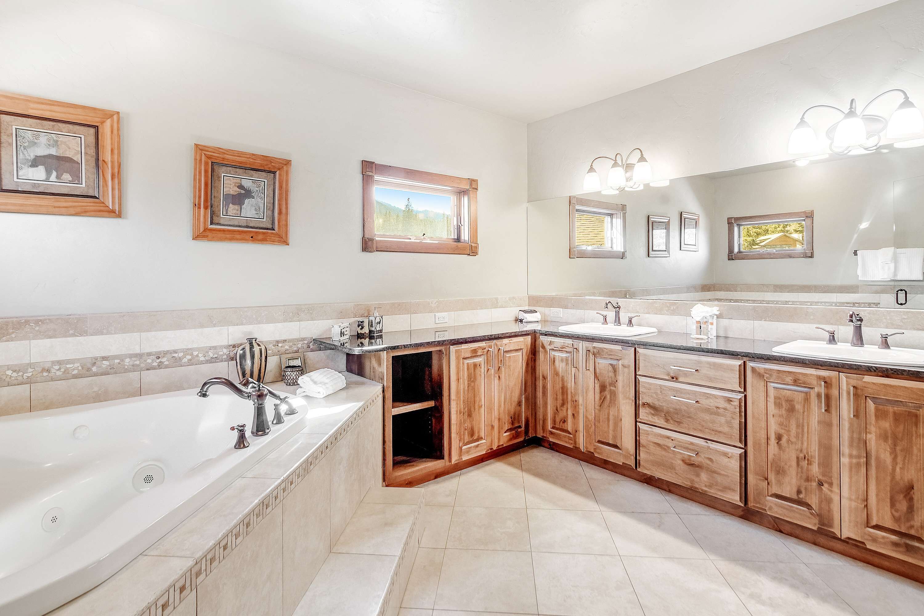 A modern bathroom with a large bathtub, wooden cabinets, and framed pictures on the wall.