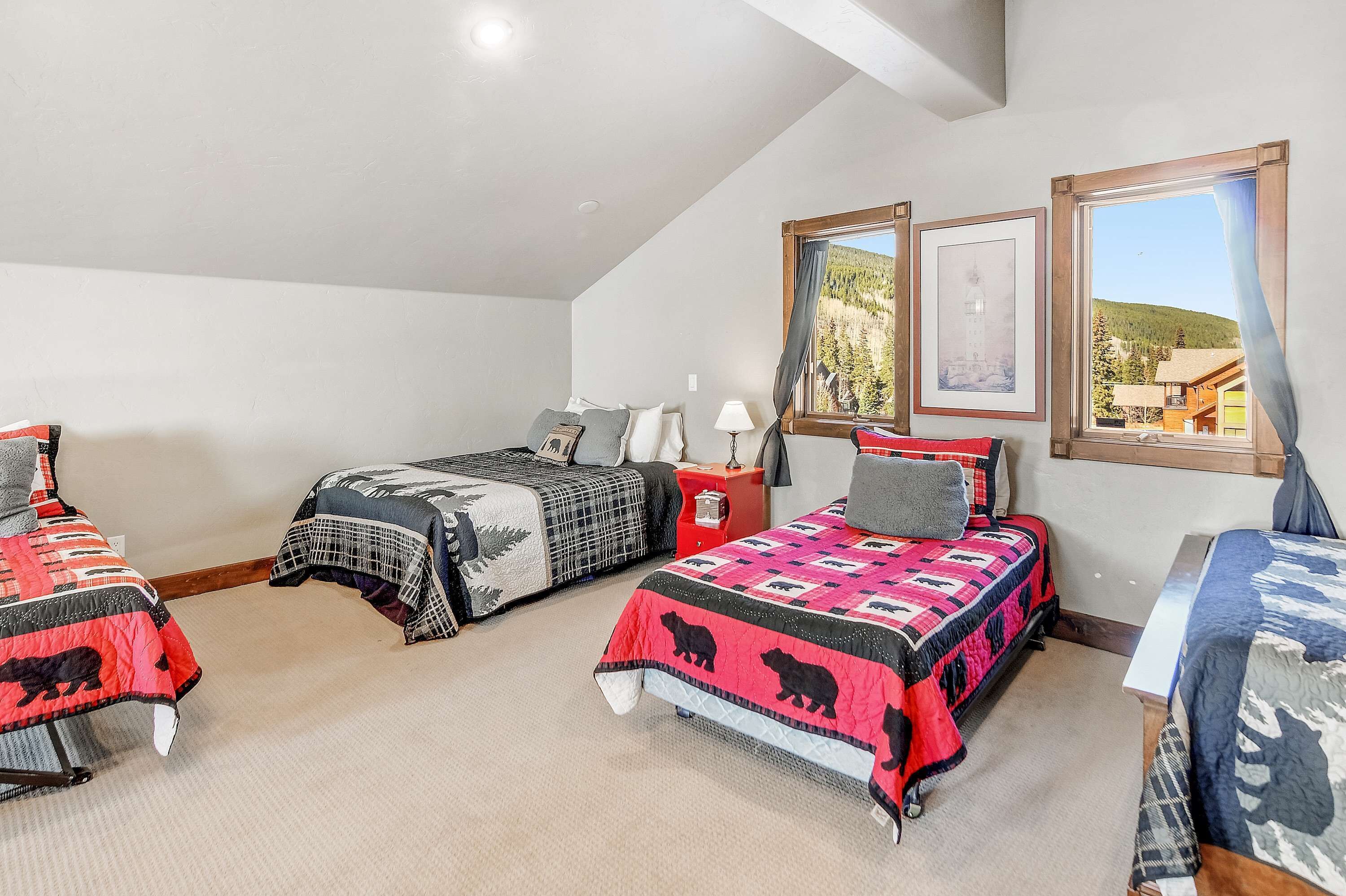A bedroom with three beds, a nightstand, a lamp, and a window with a view of a mountain.