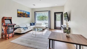 A modern living room with a sofa, a coffee table, a wooden dining table, and an NBA arcade game.