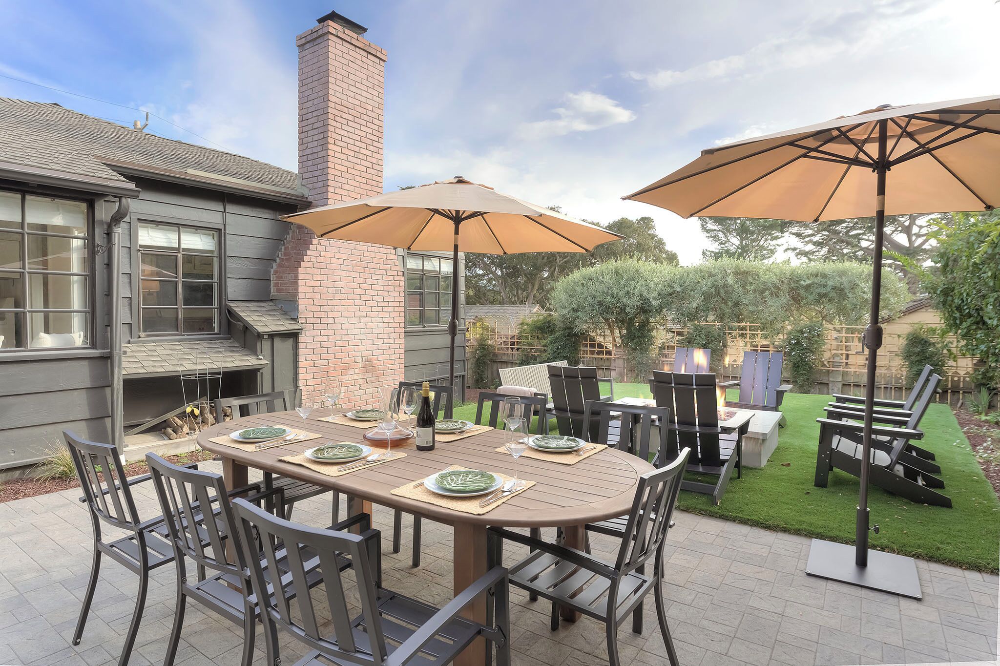 An outdoor patio with a dining table set for four, surrounded by chairs and two large umbrellas.