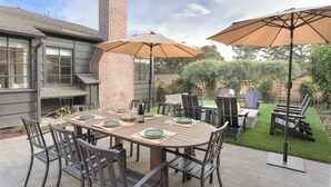 An outdoor patio with a dining table set for four, surrounded by chairs and two large umbrellas.