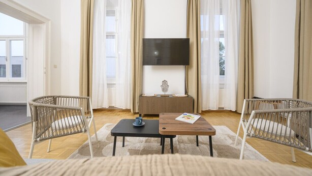 Un salon moderne avec un canapé, deux fauteuils en osier, une table basse et un téléviseur posé sur un meuble.