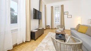Un salon moderne avec un canapé, un téléviseur, une table basse et un fauteuil en osier.