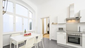 Une cuisine moderne avec des meubles blancs, un four encastré et un four à micro-ondes. On y trouve une table à manger avec des chaises et une bouteille de vin.