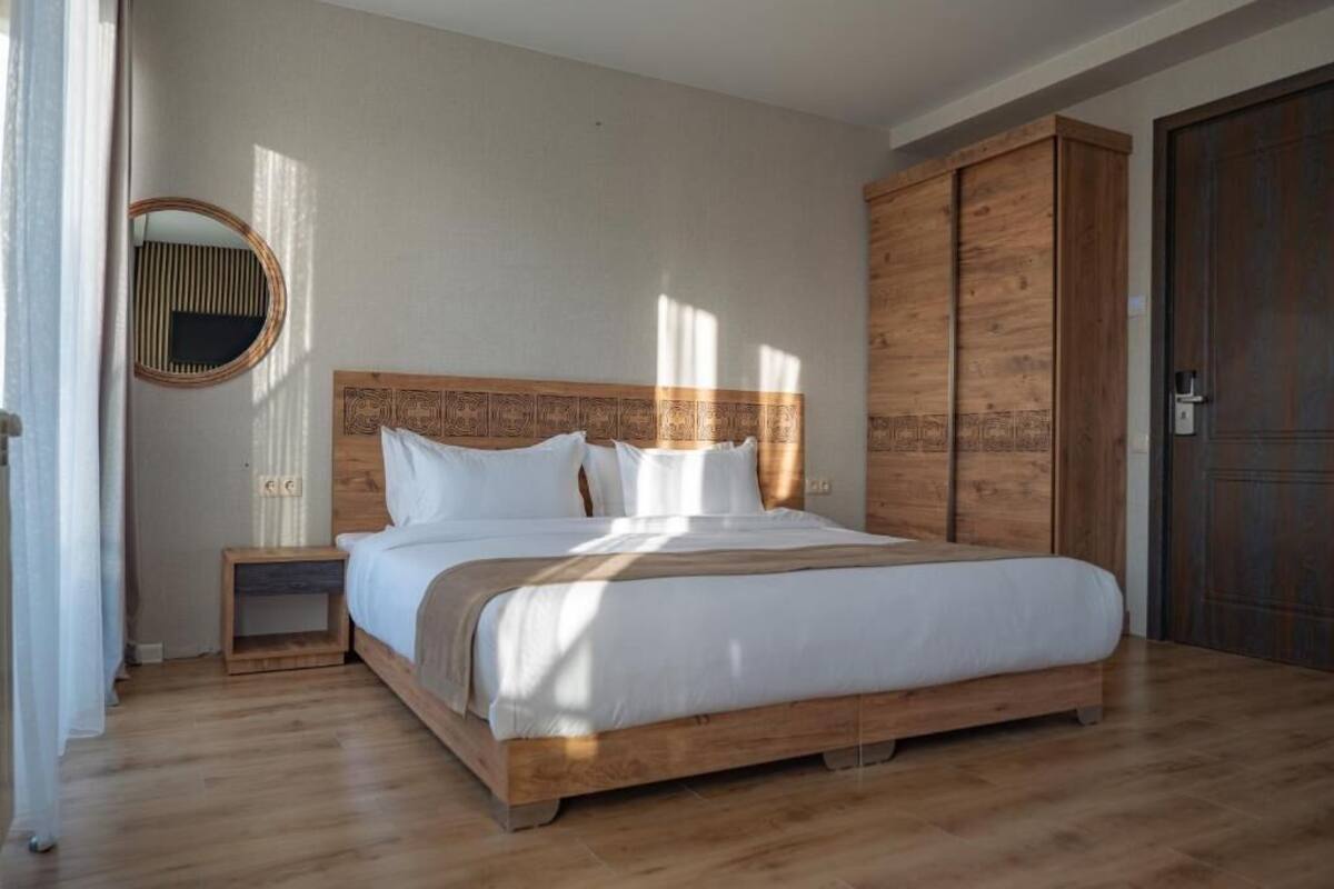 A bedroom with a wooden bed, a nightstand, a wardrobe, and a mirror on the wall.