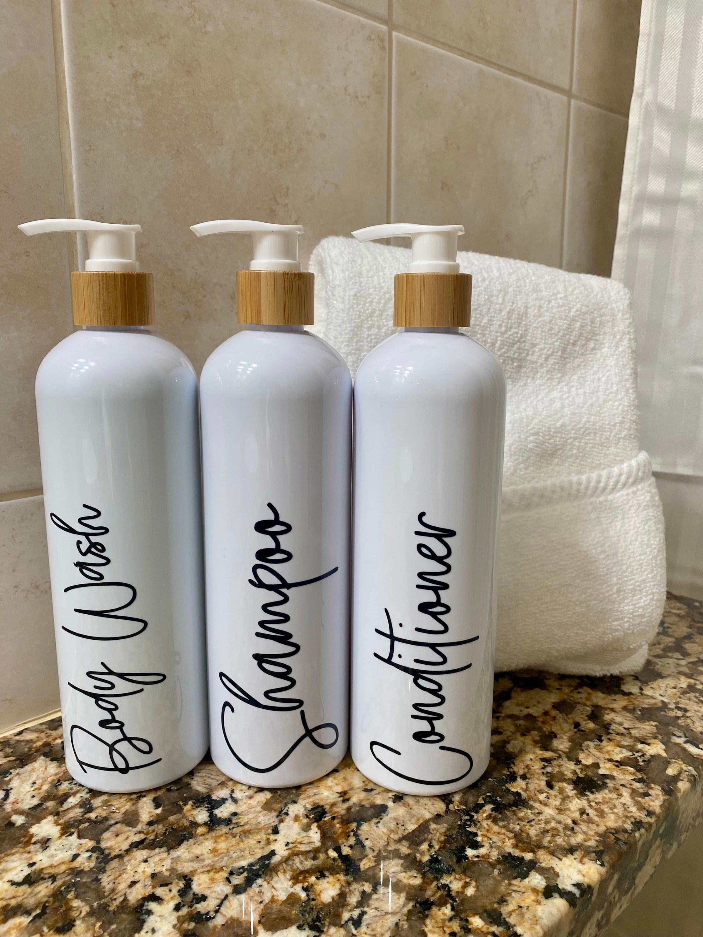 Three white bottles with pumps and labels on a granite countertop.