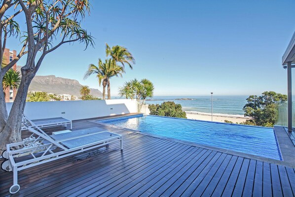 A rooftop infinity pool with lounge chairs, palm trees, and a view of the ocean.