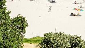 A beach with people sunbathing and walking, umbrellas, and a clear view of the ocean. - Villa Bleu Blanc in Camps Bay With Pool and Views (Cape Town)