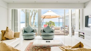 A modern living room with a large glass door leading to a balcony with a view of the sea. There are two armchairs with patterned cushions, a white sofa, and a coffee table. - Villa Bleu Blanc in Camps Bay With Pool and Views (Cape Town)