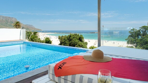 A poolside view with a beach and mountains in the background. - Villa Bleu Blanc in Camps Bay With Pool and Views (Cape Town)