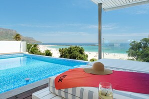 A poolside view with a beach and mountains in the background.