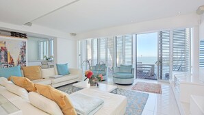 A spacious living room with a white sofa, a coffee table, and a view of the ocean through large windows. - Villa Bleu Blanc in Camps Bay With Pool and Views (Cape Town)