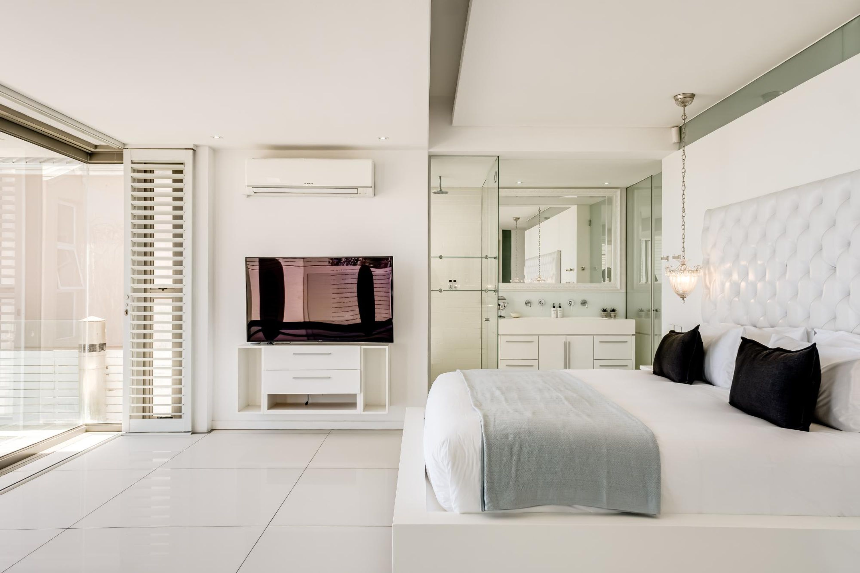 Une chambre moderne avec un grand lit, une télévision, une coiffeuse et une porte-fenêtre coulissante donnant sur un balcon.