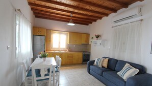 A compact kitchen with wooden cabinets, a dining table with chairs, a blue sofa, and a ceiling fan. - Villa Rouvis With Outdoor Hot Tub (Naxos)