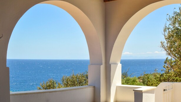 A view through a white arched structure with a wooden ceiling, overlooking a clear blue sea. - Villa Rouvis With Outdoor Hot Tub (Naxos)