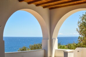 A view through a white arched structure with a wooden ceiling, overlooking a clear blue sea. - Villa Rouvis With Outdoor Hot Tub (Naxos)