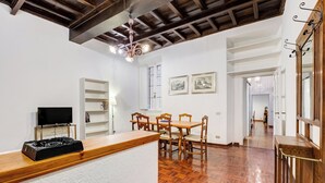 A spacious living area with a wooden dining table and chairs, a television, and a white wall with a shelf. - Spanish Steps Spacious Apartment (Rome)