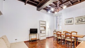 A spacious living room with a wooden floor, a sofa, a TV on a stand, a dining table with chairs, and a bookshelf. - Spanish Steps Spacious Apartment (Rome)