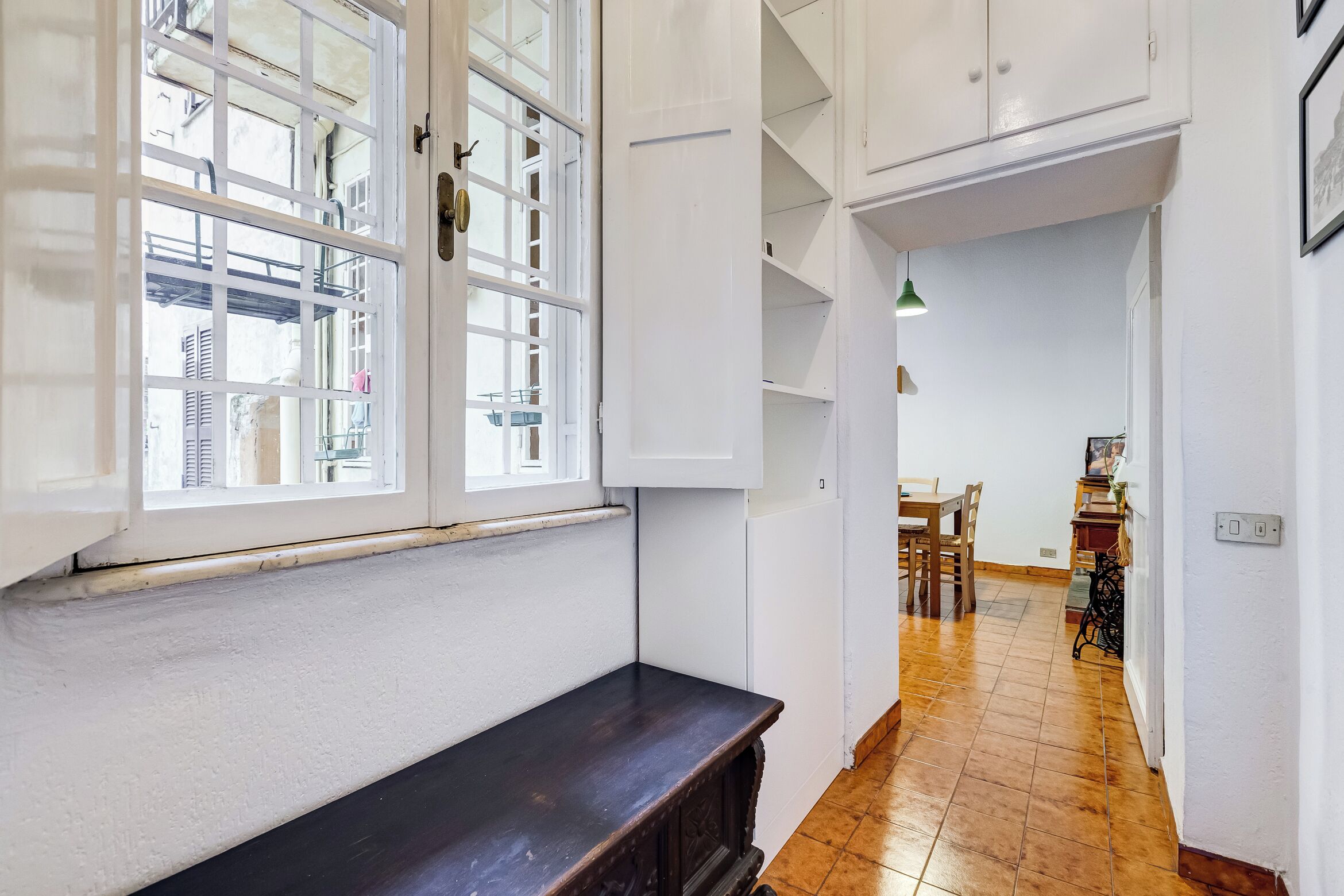 A hallway with a bench, a window, and a dining area with chairs and a table.