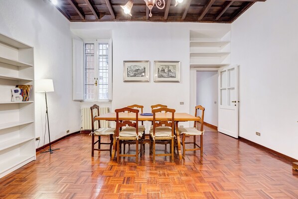 Un espace repas avec une table et des chaises en bois, des murs blancs et un parquet disposé en point de Hongrie.