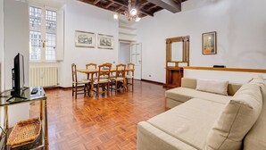 A spacious living area with a wooden floor, a sofa, a dining table with chairs, and a television on a glass table. - Spanish Steps Spacious Apartment (Rome)