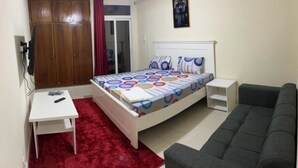 Un dormitorio con cama, escritorio, sofá, armario y ventana con cortinas.