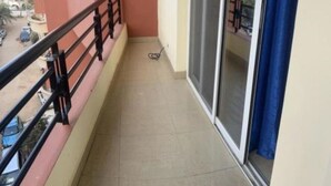Un balcón estrecho con barandilla metálica, puerta corrediza de vidrio y vista a la calle.