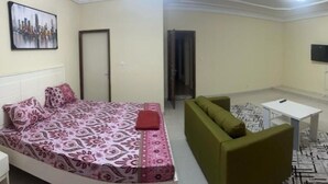 Una habitación con una cama, un sofá verde, una mesita y un televisor en la pared.