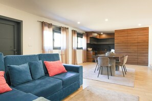 Un salon moderne avec un canapé bleu, un coin repas comprenant une table et des chaises, et une cuisine dotée de meubles en bois.