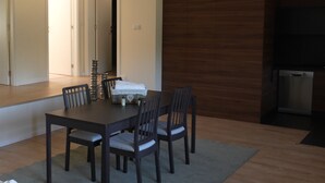 Un coin repas avec une table et des chaises en bois foncé, un petit tapis, et un espace cuisine équipé d’un lave-vaisselle.