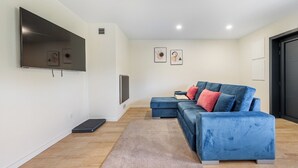 Una sala de estar moderna con un sofá azul, un televisor de pantalla plana montado en la pared y una alfombra pequeña sobre el piso de madera.
