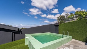 Une piscine rectangulaire dont le bord est recouvert de carreaux, entourée d’une pelouse et d’un petit muret.