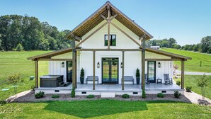 A two-story house with a covered porch, a hot tub, and a small garden area.