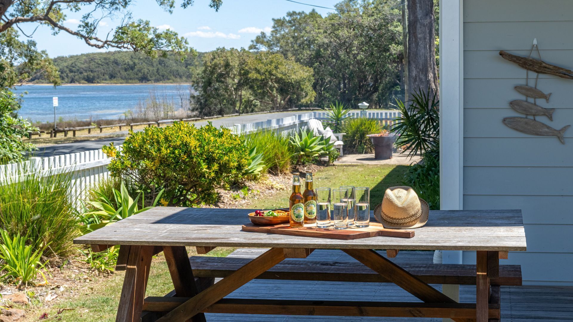 A wooden picnic table with a bottle of beer, glasses, and a hat on it.