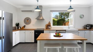 Una cocina moderna con armarios blancos, encimera de madera, horno empotrado, lavavajillas y un amplio ventanal que proporciona luz natural.