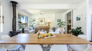 Un comedor con mesa de madera, sillas blancas y una isla central con lámpara y adornos.