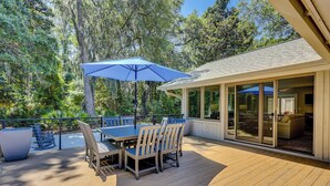 A wooden deck with a table and chairs, a blue umbrella, and a glass door leading to an interior space.