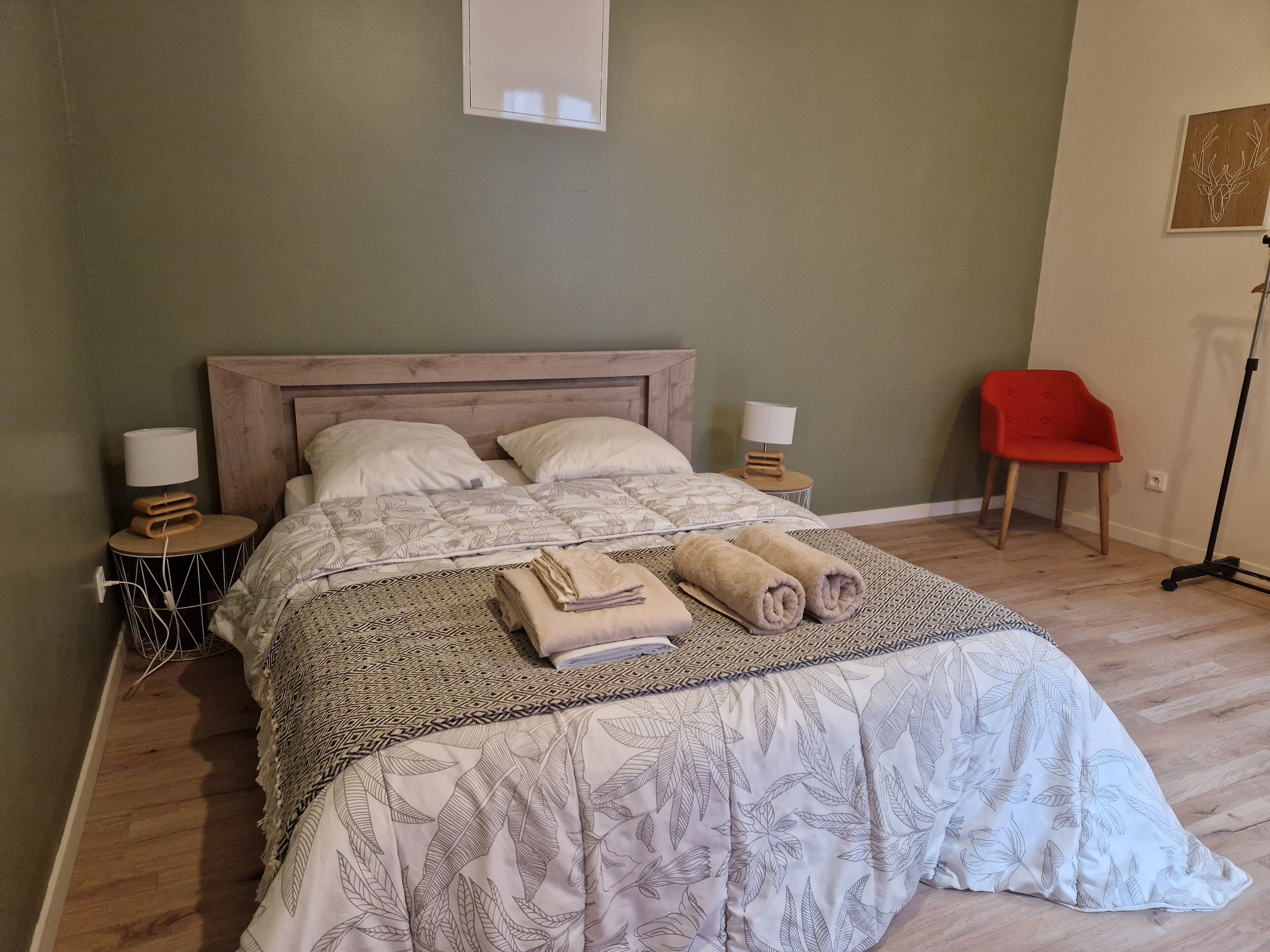 A neatly made bed with a patterned bedspread and pillows, two bedside lamps, a red chair, and a floor lamp.