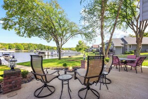 An outdoor patio with chairs and a table, a fire pit, and a view of a lake and buildings.