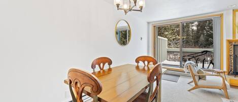 A dining area with a wooden table and chairs, a chandelier, a large mirror, and a view of bicycles outside.