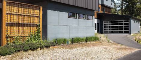 A modern two-story house with a garage, a gravel driveway, and a wooden fence with climbing plants.