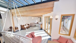 Une pièce spacieuse avec un fauteuil suspendu, un canapé rose et une table en bois.