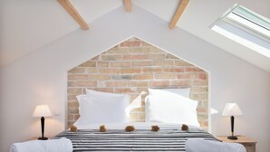 Une chambre avec un plafond en pente, un mur en briques, un lit avec une literie à rayures, deux lampes de chevet et un puits de lumière.