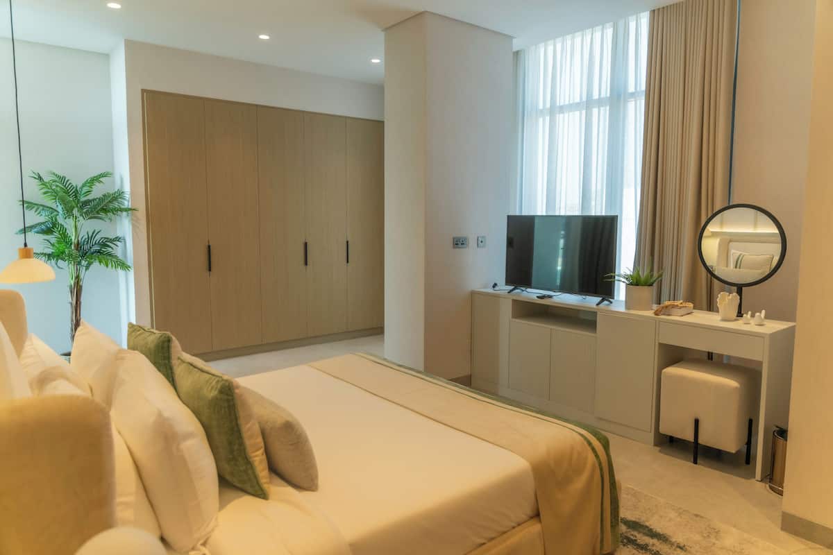 A modern hotel room with a large bed, a desk with a TV, a mirror, and a wardrobe.