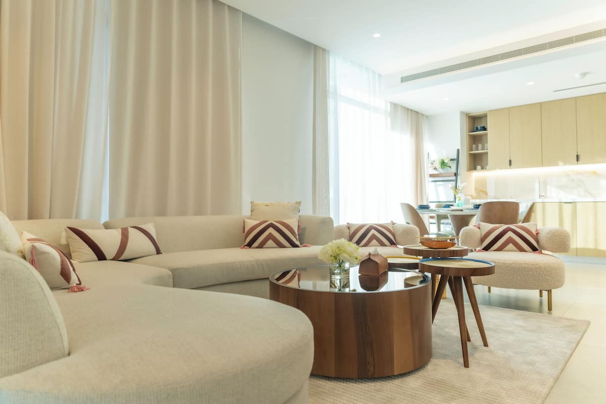 A modern living room with a sectional sofa, a round coffee table, and a dining area with chairs and a kitchen in the background.