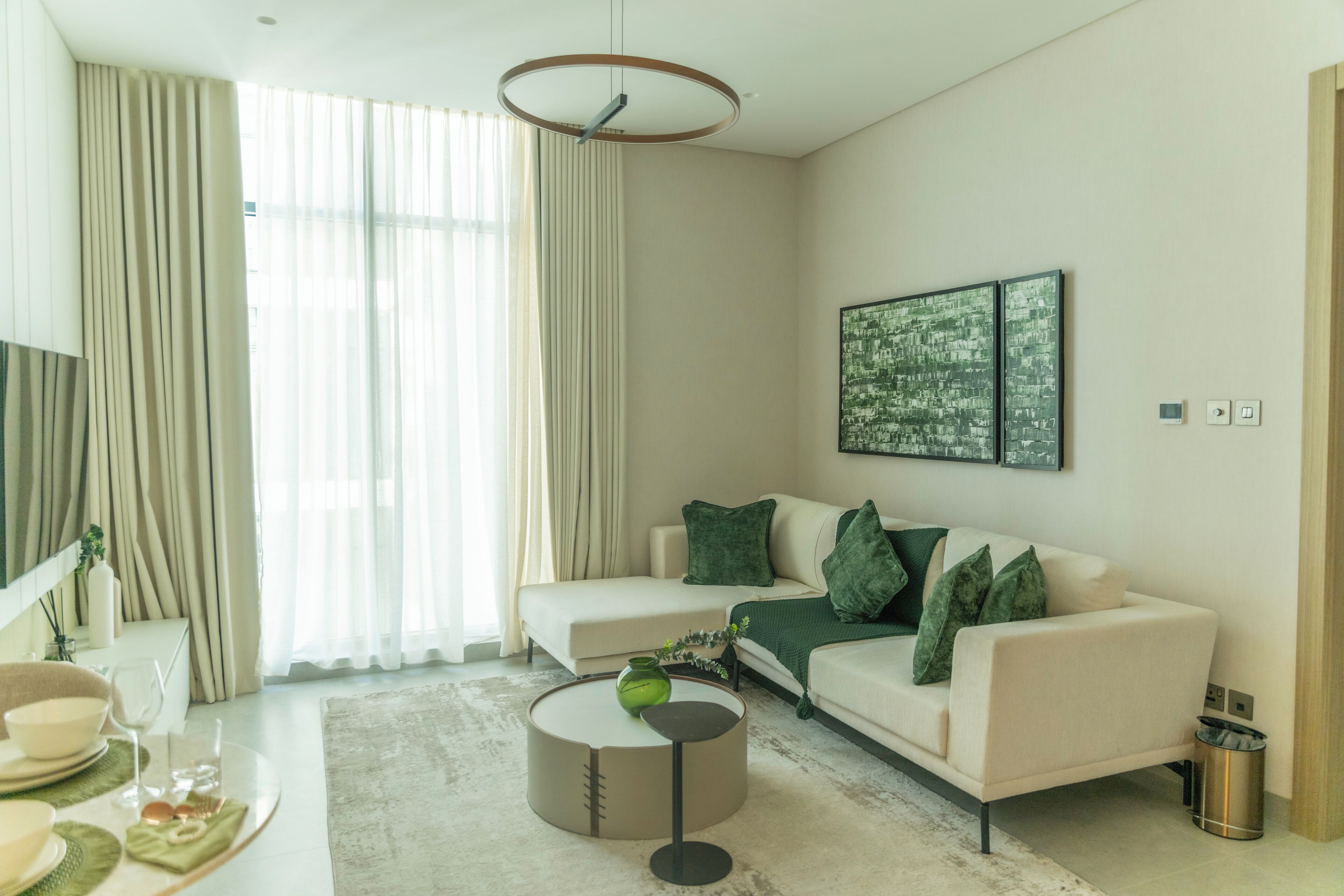 A modern living room with a beige sofa, a round coffee table, and a large window with curtains.