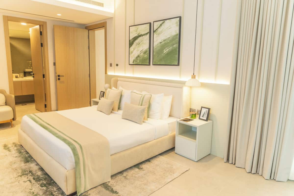 A modern hotel room with a large bed, bedside tables, a nightstand, a mirror, and a wardrobe.